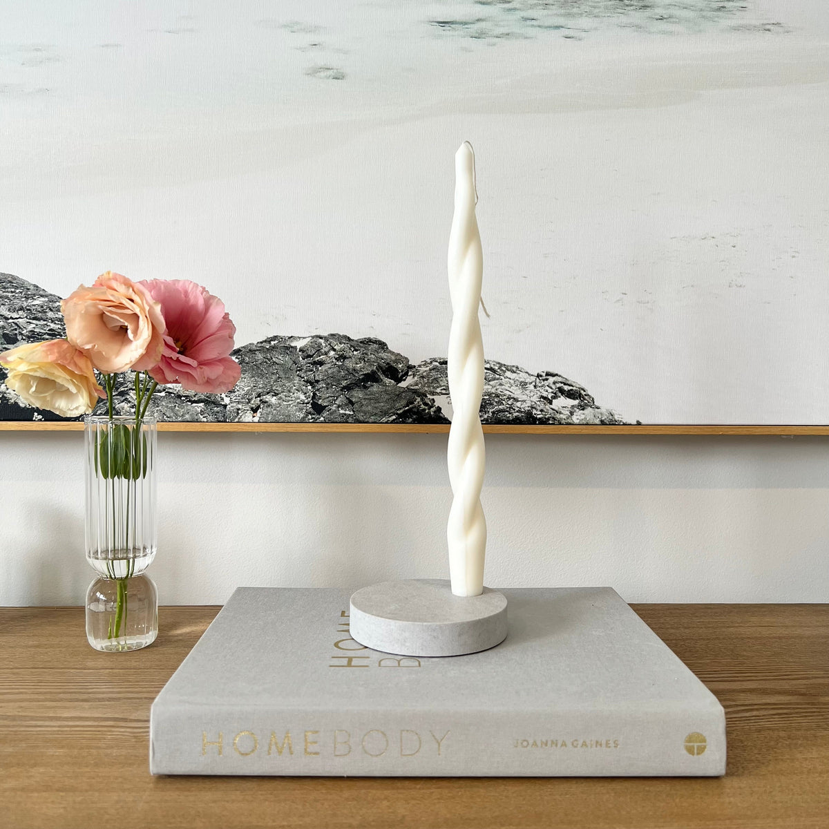 Quartz Round Single Candle Holder in Caesarstone Airy Concrete created by Aureliia Collection. Styled with Studio McKenna Chunky Twist Taper pillar candle and vase with flowers on timber table. This candle holder has a feel of concrete in full movement. The perfect home decor item.