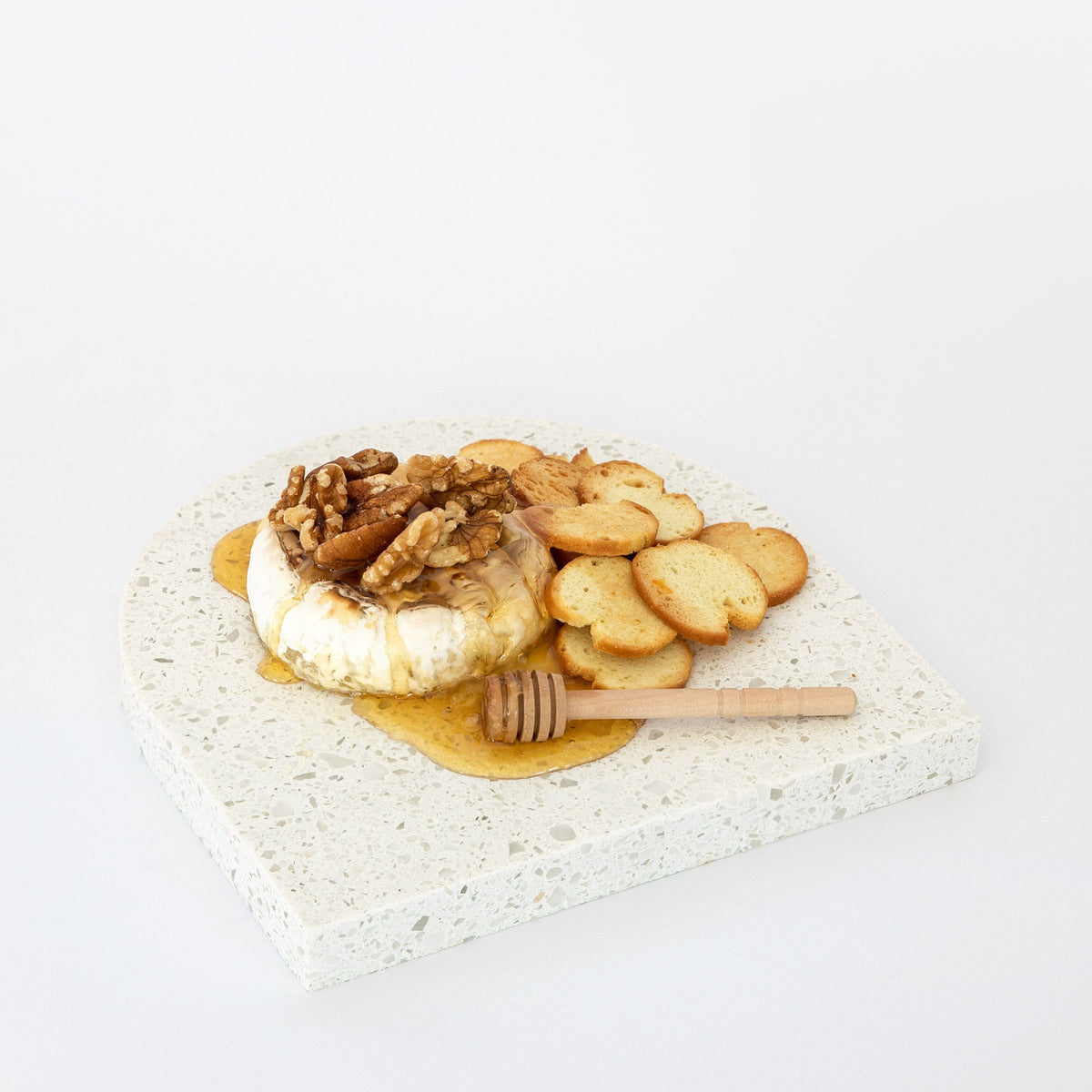 Quartz Arch Platter in Caesarstone Nougat created by Aureliia Collection. Styled with baked Camembert cheese, crackers an walnuts drizzled with honey. This decorative quartz serving platter is chunky coarse-grained textures and neutral-coloured mineral chips, on a classic white canvas. Platters are functional multipurpose items made from quartz which is more resilient and scratch proof in comparison to marble platter.