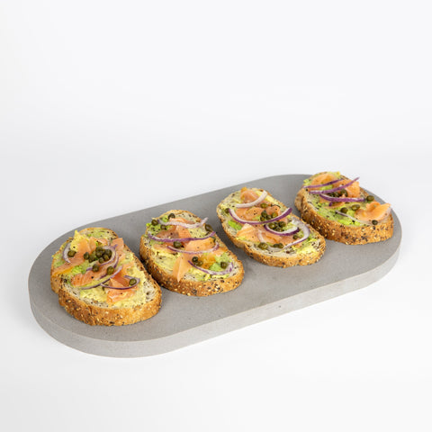 Double arch quartz platters in Caesarstone Sleek Concrete™ created by Aureliia Collection. The Double arch quartz platter shown with salmon and avocado open sandwiches topped with thin sliced red onion and capers. An excellent home decor gift for someone who has it all.