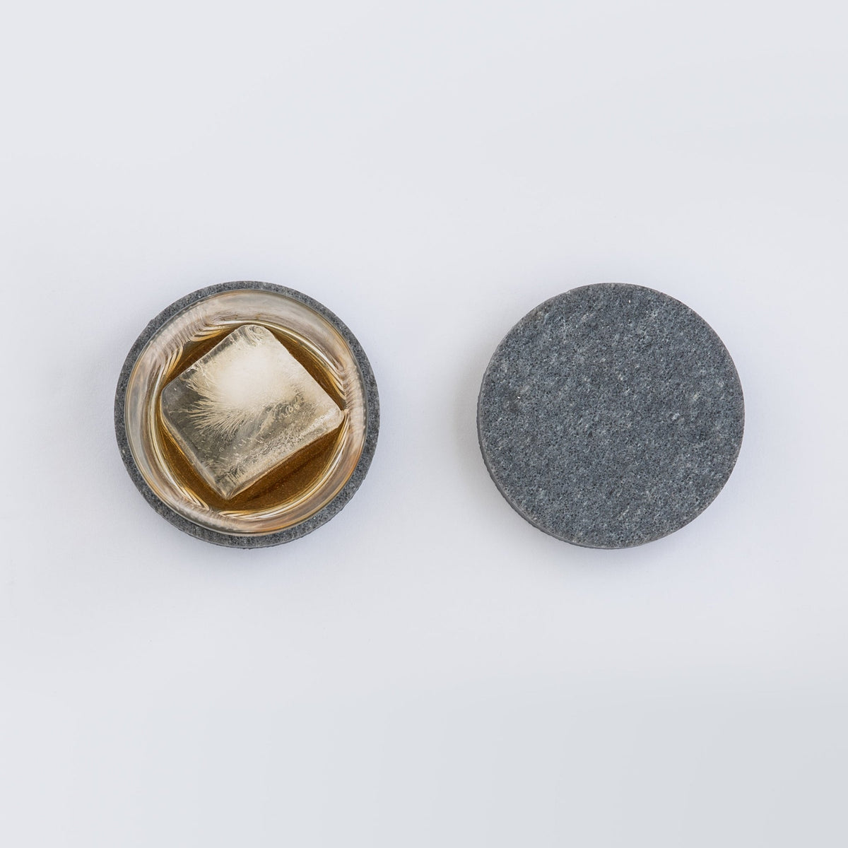 Round thick coaster in Caesarstone 4033 Rugged Concrete. Shown with whiskey glass and large ice cube.