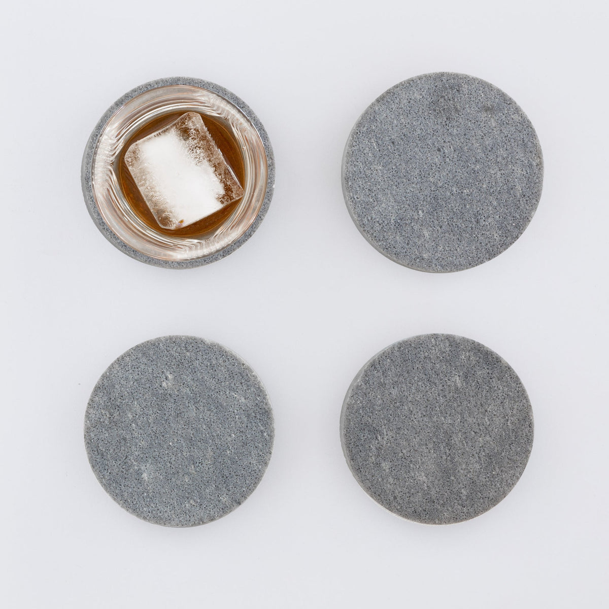 4 round marble like coasters in Caesarstone 4033 Rugged Concrete. Shown with whiskey glass and large ice cube.