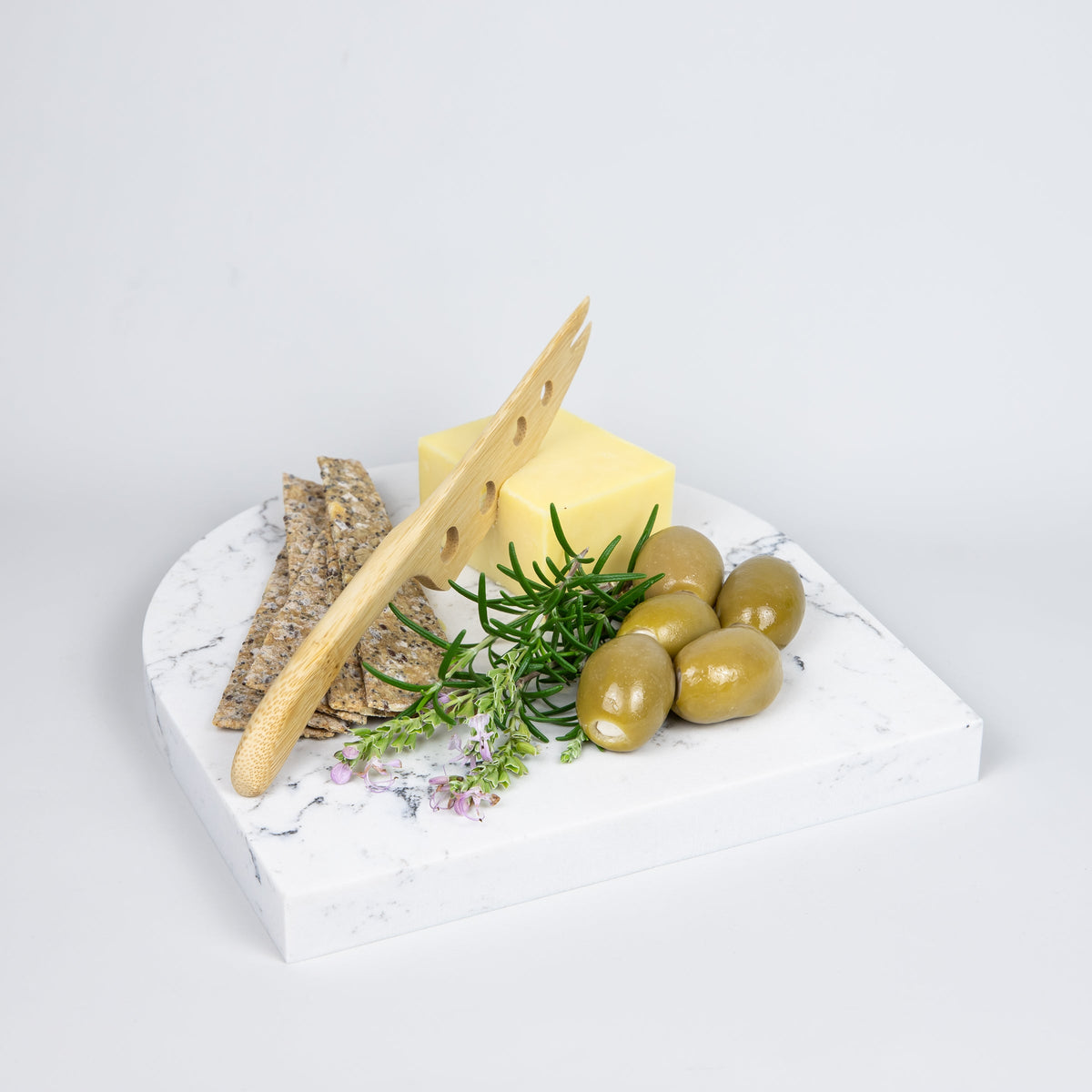 Quartz Arch Platter in Caesarstone White Attica created by Aureliia Collection. Styled with cheese, feta stuffed olives, crackers and rosemary. This decorative quartz serving platter has an alluring combination that overflows with the rush of grey tones, ebbing across a flawless white base. Platters are functional multipurpose items made from quartz which is more resilient and scratch proof in comparison to marble platter.