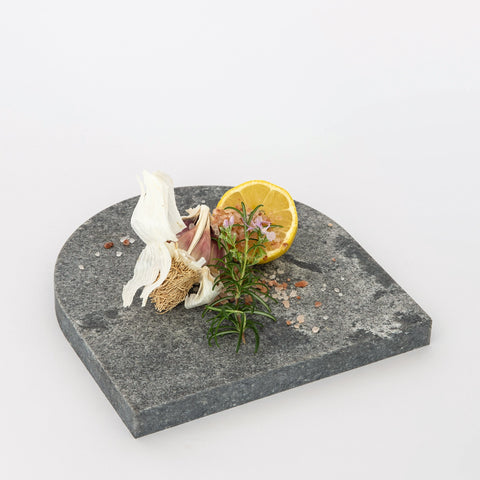 Quartz Arch Platter in Caesarstone Rugged Concrete created by Aureliia Collection. Styled with garlic cloves, sea salt, lemon half and rosemary. This decorative quartz serving platter is dramatic gradients of robust greys, flashed with white-haze patinas and accentuated with industrial-inspired imperfections. Platters are functional multipurpose items made from quartz which is more resilient and scratch proof in comparison to marble platter.