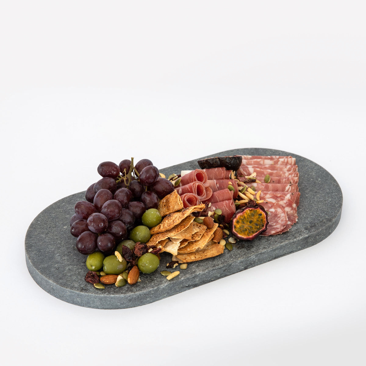 Double arch quartz platters in Caesarstone Rugged Concrete™ created by Aureliia Collection. The Double arch quartz cheese boards shown with salami, prosciutto, Sicilian olives, red grapes, cut passionfruit and pita crackers. An excellent home decor gift for someone who has it all.