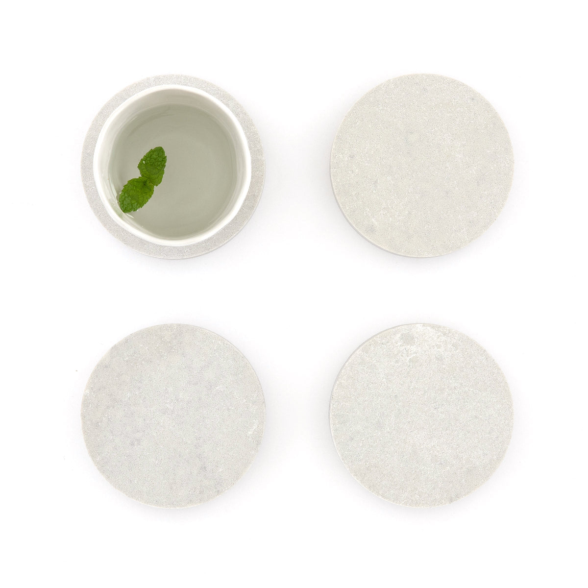 Round quartz coasters in Caesarstone Airy Concrete™ created by Aureliia Collection. Similar to a marble, the Round Quartz Coasters shown with glass of water, featuring mint leaf. An excellent home decor gift for someone who has it all.