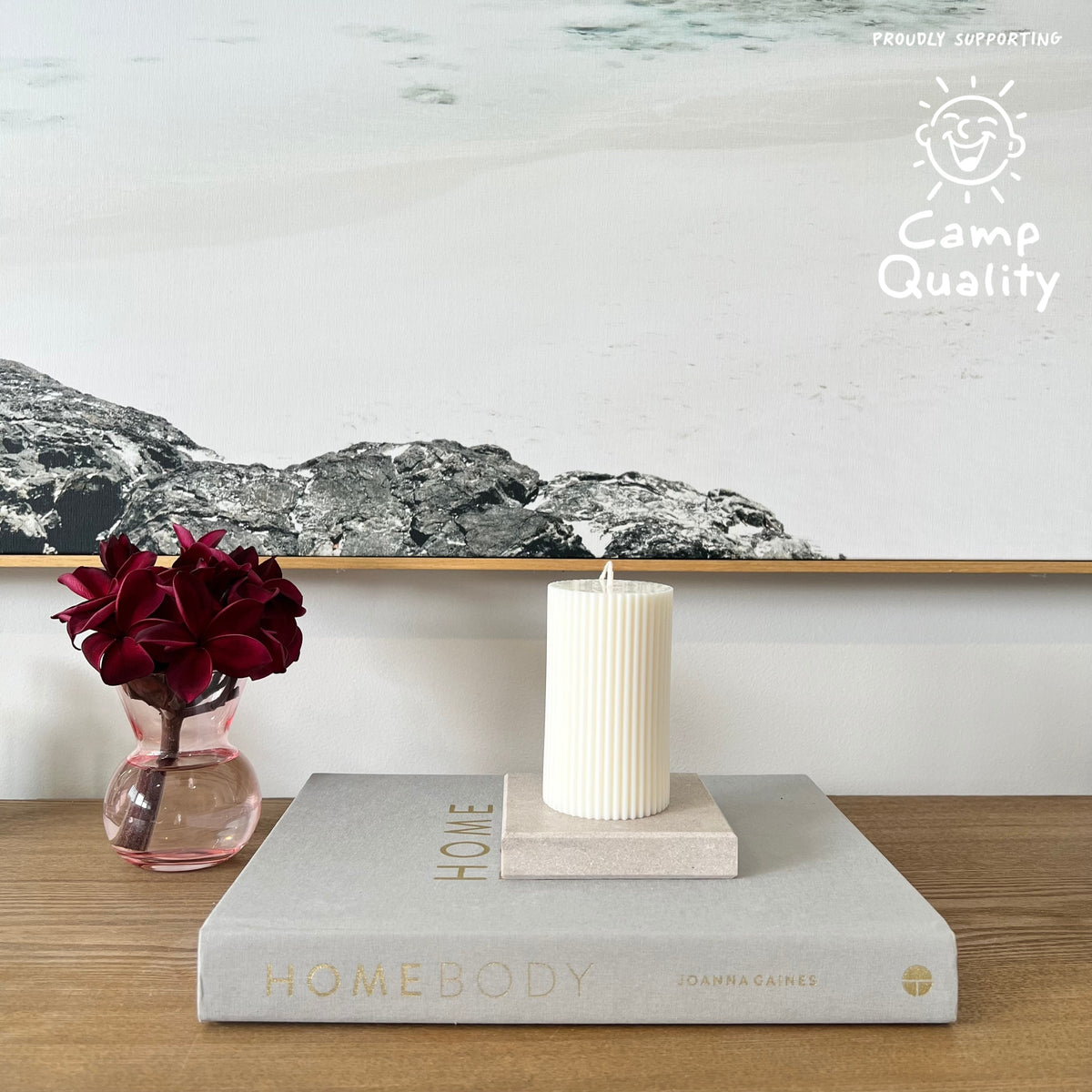 Quartz Square Candle Holder in Caesarstone Topus Concrete created by Aureliia Collection. Styled with Studio McKenna white pillar candle, upon Joanna Gaines book  next to vase with fresh flowers on timber table. This candle holder has full of movement, opacity, and depth of delicate mineral formations over a warm greige base, flushed with rugged patinas and pastel-pink undertones. The perfect home decor item.