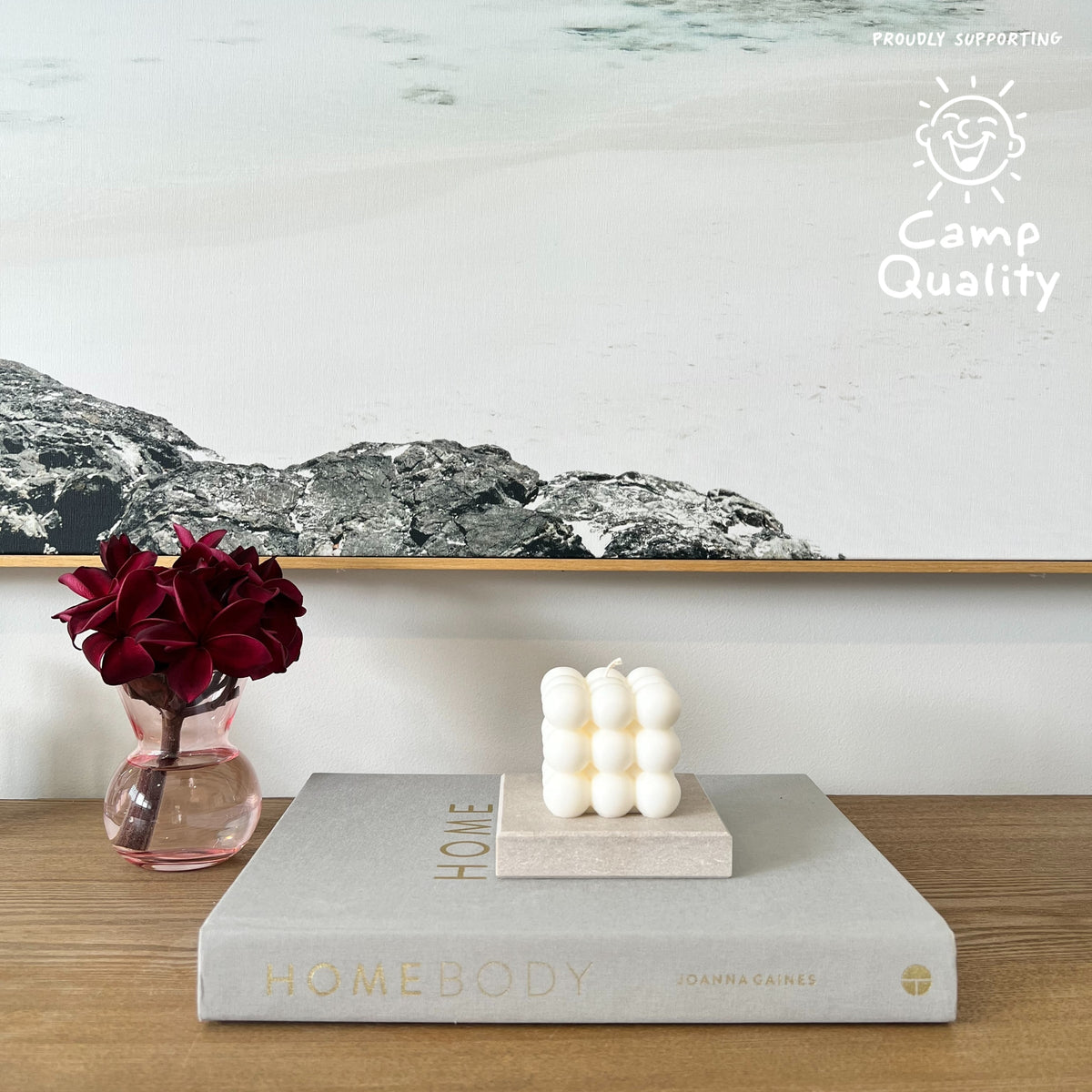 Quartz Square Candle Holder in Caesarstone Topus Concrete created by Aureliia Collection. Styled with Studio McKenna No. 27 candle, upon Joanna Gaines book  next to vase with fresh flowers on timber table. This candle holder has full of movement, opacity, and depth of delicate mineral formations over a warm greige base, flushed with rugged patinas and pastel-pink undertones. The perfect home decor item.